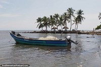 Fishing boat, palms and thatched umbrellas on the seafront in Necocli.