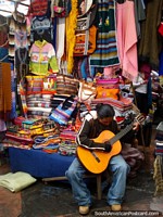 Bright colored bags and clothing with guitar playing salesman in Otavalo. Ecuador, South America.