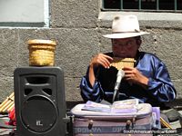 Larger version of Man busking in Quito, playing pipes on the footpath.