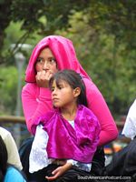 Local woman and girl of Quito in purple and pink in park El Ejido.