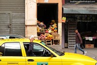 Fruit and vegetable shop, boy walks past, yellow taxi, Ambato. Ecuador, South America.