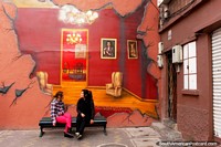Wall mural of a lounge scene, 2 girls talk in front of it, Ambato. Ecuador, South America.