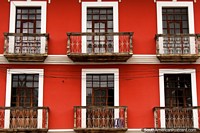 Bien cuidado edificio rojo con balcones de madera y de hierro y ventanas limpias en Guaranda. Ecuador, Sudamerica.
