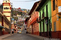 A colorful street in Guaranda with houses and a church with houses on the hills in the distance.