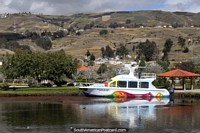 A colorful boat sits on the water at Colta Lagoon with hills in the background. Ecuador, South America.