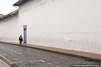 El hombre pasa junto a una puerta azul a lo largo de una pared blanca larga en Cuenca. Ecuador, Sudamerica.