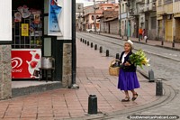 A woman wearing a white hat carries flowers along the street in Cuenca. Ecuador, South America.