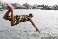 O jovem voa na água depois de saltar do cais em San Lorenzo. Equador, América do Sul.