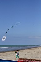 O rapaz voa um pequeno papagaio de papel em um grande céu na praia em El Matal. Equador, América do Sul.