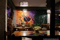 Painting of a beach girl carrying a surfboard while riding a bike inside a restaurant in Montanita.