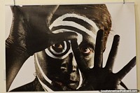 Versión más grande de Hombre negro con pintura blanca en la cara y dedos extendidos, foto en el centro cultural de Loja.