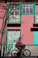 Fachada rosada de una casa con ventanas y puertas verdes, hombre en bicicleta, Banos. Ecuador, Sudamerica.