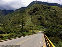 A via das cachoeiras toma-o através desta ponte com enormes montanhas adiante em Banos. Equador, América do Sul.