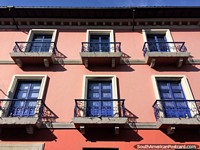 Fachada rosa ao sol com portas azuis e balcões de ferro, Quito central.