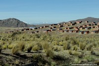 Versão maior do Pequenos edifïcios de tijolos e montanhas nevosas na distância em volta de Desaguadero, a cidade de borda dual do Peru e a Bolïvia.