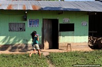 Girl runs home with a bottle of something, simple house in the Amazon around Aguaytia. Peru, South America.
