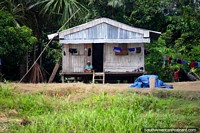 A woman sits on the porch of her wooden Amazon house watching river-life go by between Iquitos and Santa Rosa. Peru, South America.
