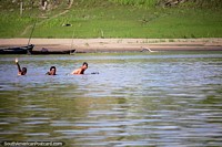 Locals of the Amazon wave while they swim in the river, west of Santa Rosa and the border. Peru, South America.