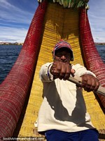 O homem que tem 6 famïlias rema o seu barco de dragão através do Lago Titicaca em Puno. Peru, América do Sul.