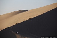 People ascend to the peaks of the dunes for sunset in Huacachina. Peru, South America.