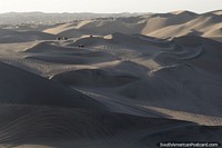 Vast sand dunes dwarf the dune buggies that cruise around them in Huacachina. Peru, South America.