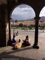 Fluffy brown alpaca sits with her owners in an archway at the plaza in Cusco. Peru, South America.