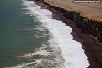 Waves come crashing in and sweep up red stone beach at Paracas National Park. Peru, South America.
