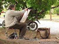 Um artista senta-se no prefeito de Praça pública que desenha um quadro do farol na Colônia. Uruguai, América do Sul.