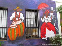 Um lado de edifïcio pintou com pessoas coloridas, homem com bongôs, mulher com o guarda-chuva, Colônia. Uruguai, América do Sul.