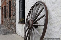 Versión más grande de Una rueda de carro de madera vieja se encuentra en una calle con bonitas fachadas en Colonia del Sacramento.