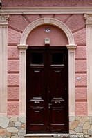 Fachada rosa con una puerta de madera oscura, un arco y columnas en Paysandú. Uruguay, Sudamerica.