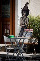 Extraña figura se encuentra fuera de una tienda con una mesa y una silla en Colonia del Sacramento. Uruguay, Sudamerica.