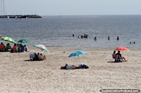 People enjoy the beach and waters in Piriapolis while people sail in the distance. Uruguay, South America.