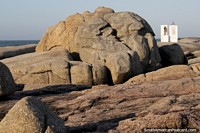 Large boulder in the shape of a brain and the distant lighthouse monument at Punta del Diablo. Uruguay, South America.