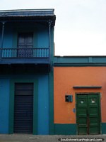 Edificio azul con balcón siguiente a construcción con una puerta de madera verde, Puerto Cabello. Venezuela, Sudamerica.