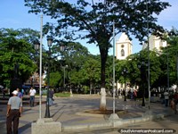 Versión más grande de Plaza Bolivar en Porlamar con monumento, iglesia, árboles y lámparas.