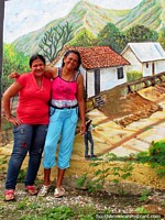 2 local women pose for a photo in front of a wall mural in El Tintorero. Venezuela, South America.