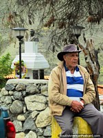 A local man with hat of Mucuchies sits beside a stone wall and the plaza. Venezuela, South America.