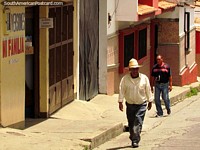 Larger version of Local man of Timotes walks up the street with his hat on.