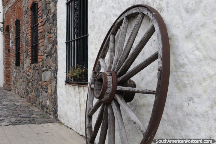 An old wooden wagon wheel stands on a street with nice facades in Colonia del Sacramento. (720x480px). Uruguay, South America.