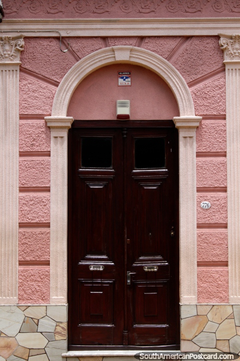 Fachada rosa con una puerta de madera oscura, un arco y columnas en Paysand. (480x720px). Uruguay, Sudamerica.