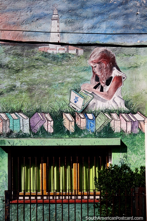 La nia se sienta en la hierba con libros y un faro lejano, mural en Punta del Este. (480x720px). Uruguay, Sudamerica.