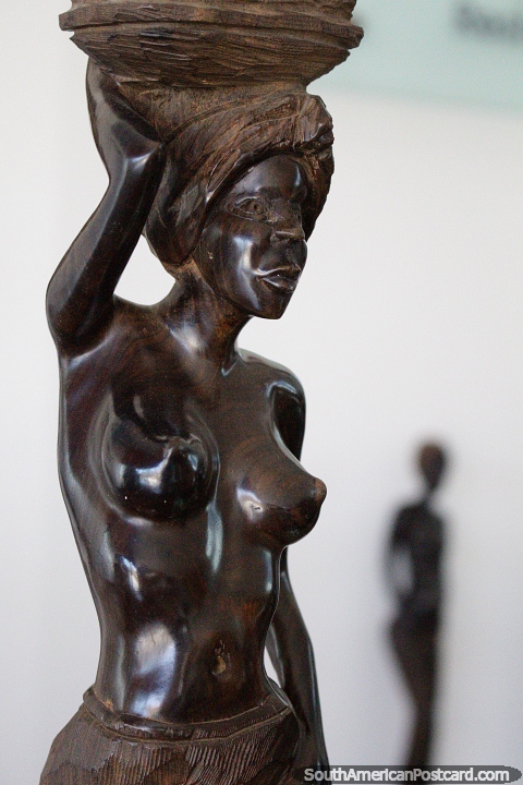 Carved, smoothed and polished, wooden sculpture of a woman with basket on her head, art in Punta del Este. (480x720px). Uruguay, South America.