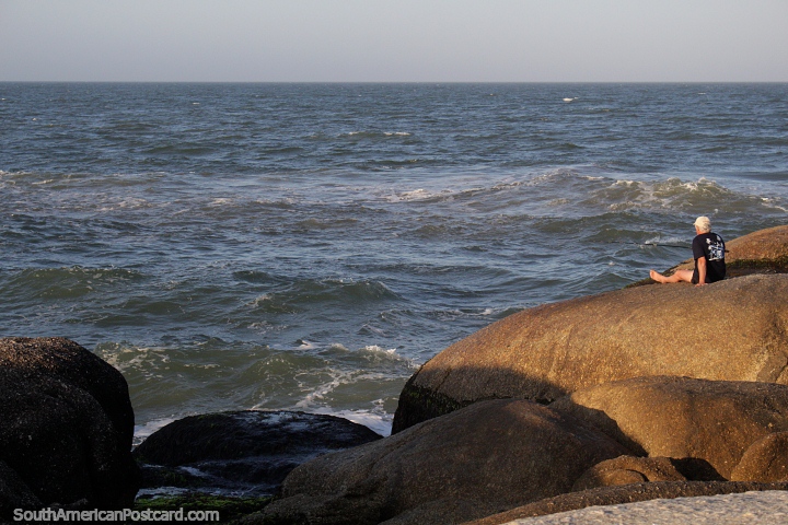 Homem que pesca de um grande seixo rolado em Punta do Diablo, o mar é agitado. (720x480px). Uruguai, América do Sul.