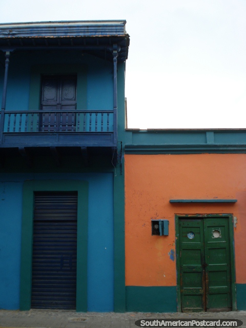 Edificio azul con balcón siguiente a construcción con una puerta de madera verde, Puerto Cabello. (480x640px). Venezuela, Sudamerica.