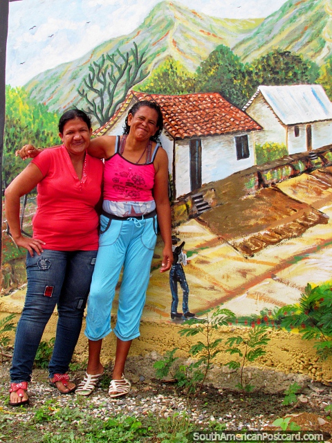 2 mujeres locales posan para una foto delante de una mural en la pared en El Tintorero. (480x640px). Venezuela, Sudamerica.