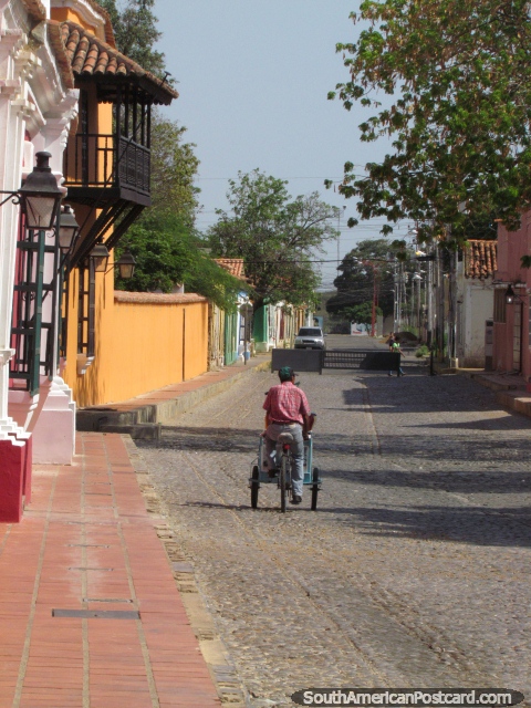 O homem anda em uma carreta da bicicleta ao longo de uma rua de pedra arredondada em Coro central. (480x640px). Venezuela, América do Sul.