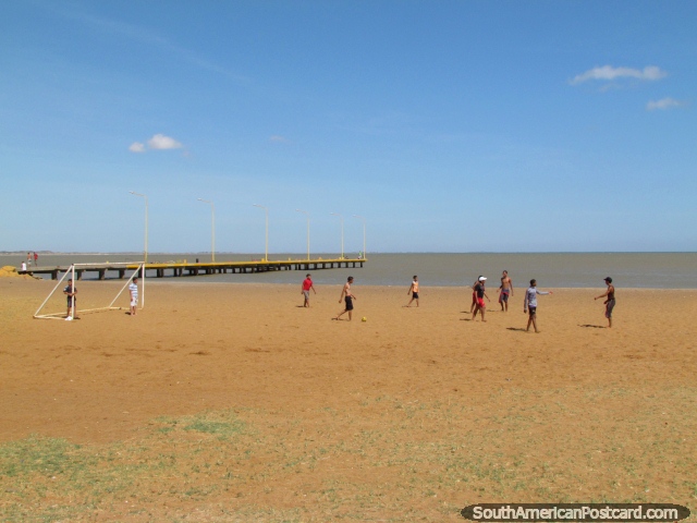 Os rapazes jogam o futebol na areia perto do cais em La Vela de Coro. (640x480px). Venezuela, América do Sul.
