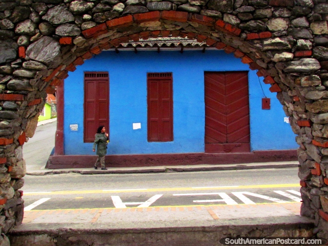 Looking through a stone arch at a blue facade with brown wooden doors in Mucuchies. (640x480px). Venezuela, South America.